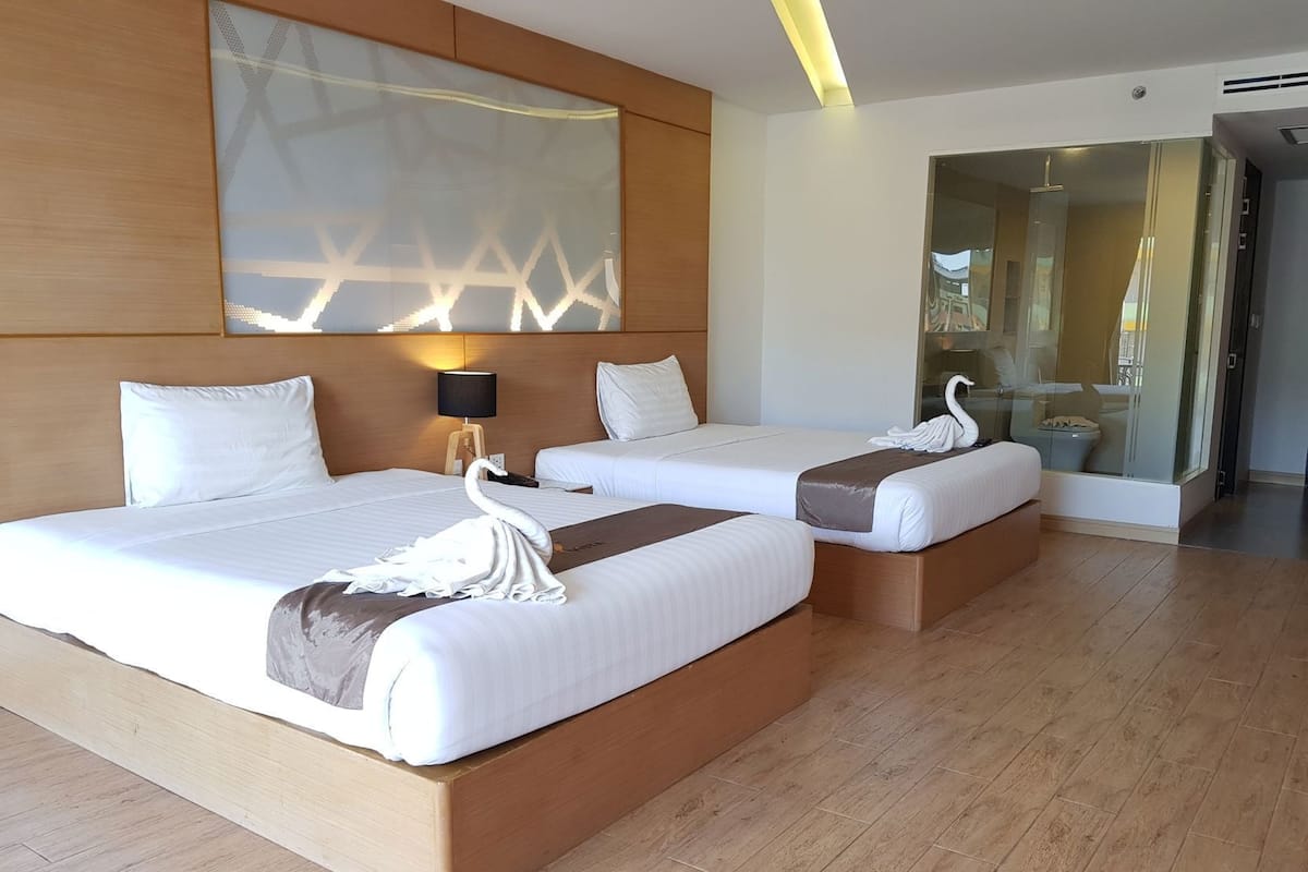 A hotel room with two beds, a wooden headboard, a wall-mounted lamp, and a glass shower enclosure.