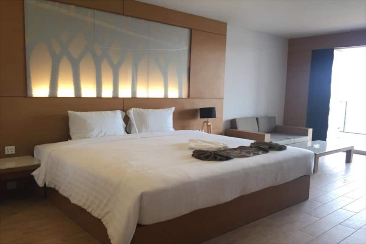 A large bed with white linens, a nightstand, a lamp, and a view of the outdoors.