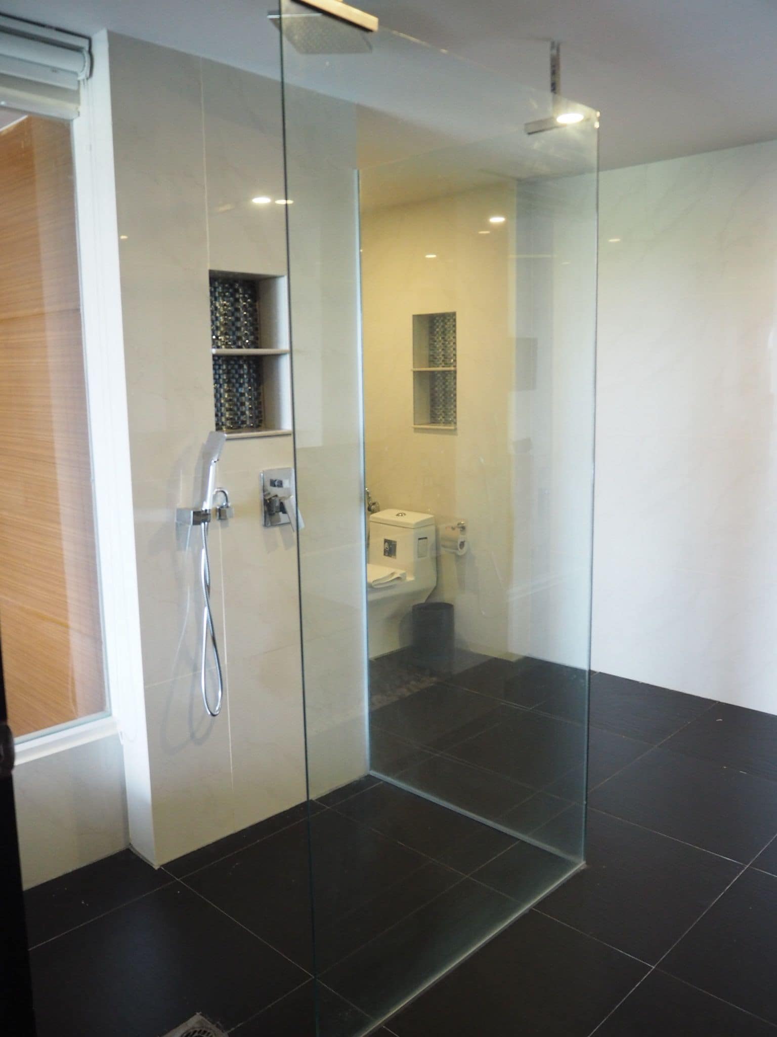 Un baño moderno con cabina de ducha de vidrio, suelo de baldosas oscuras y lavabo blanco.
