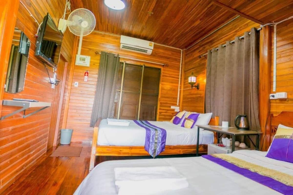 A wooden room with two beds, a fan, an air conditioning unit, and a small table with a kettle.