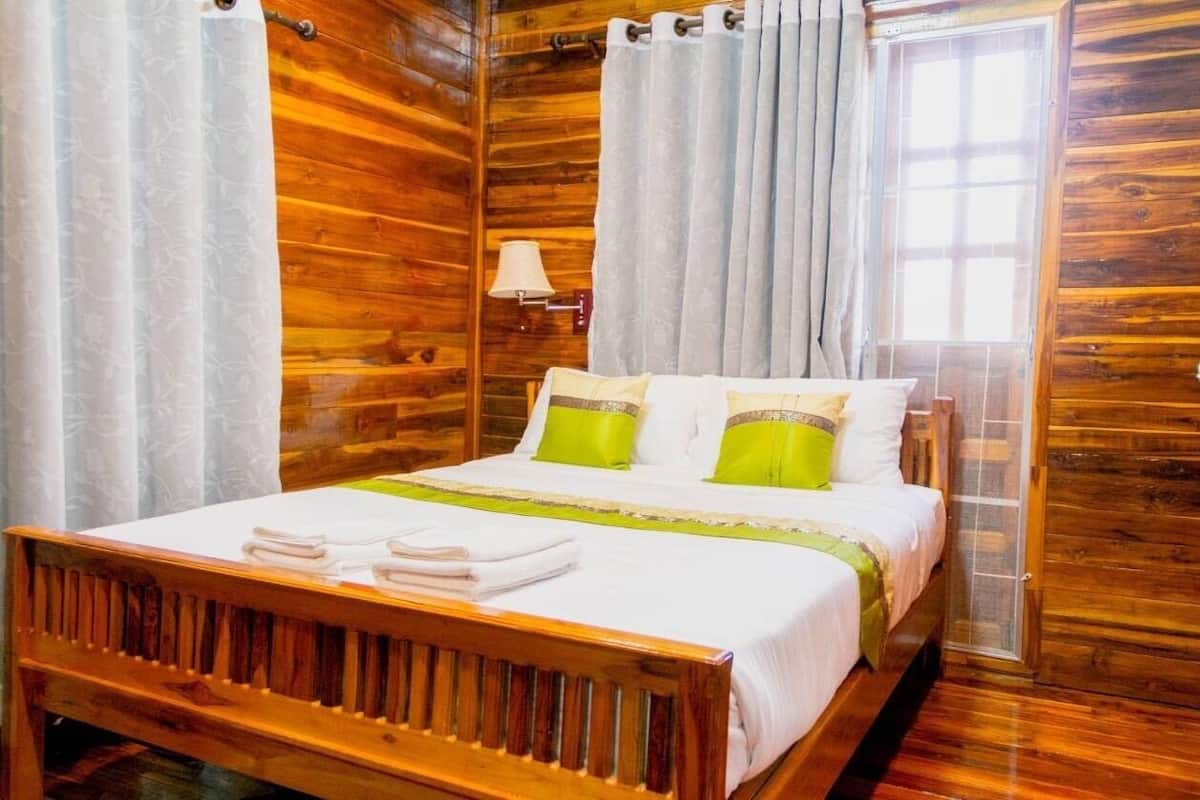 A wooden-paneled room with a bed, curtains, a lamp, and a window.