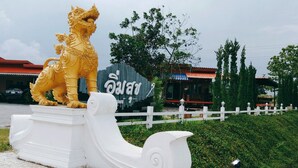 Eine goldene Löwenstatue auf einem Sockel, ein weißes Geländer und ein Gebäude mit rotem Dach im Hintergrund.