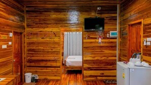 Ein Zimmer in einer Holzhütte mit einem Bett, einem Fernseher, einer Mikrowelle und einem Kühlschrank.