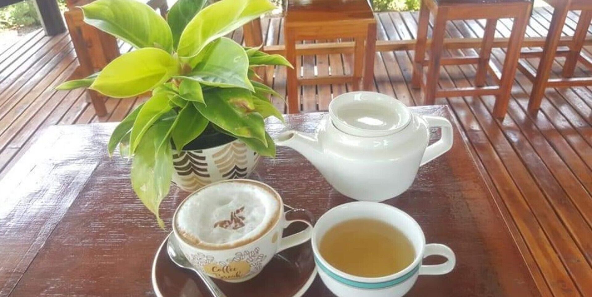 Una mesa de madera con un hervidor, una taza de té y una taza de café con su platito.