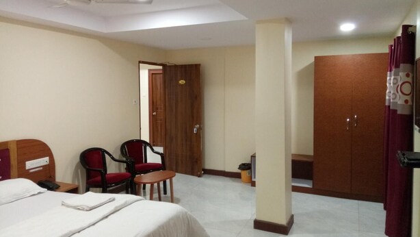 A hotel room with a bed, two chairs, a small table, a wardrobe, and a ceiling fan. - Sunnyvale Andaman (Port Blair)