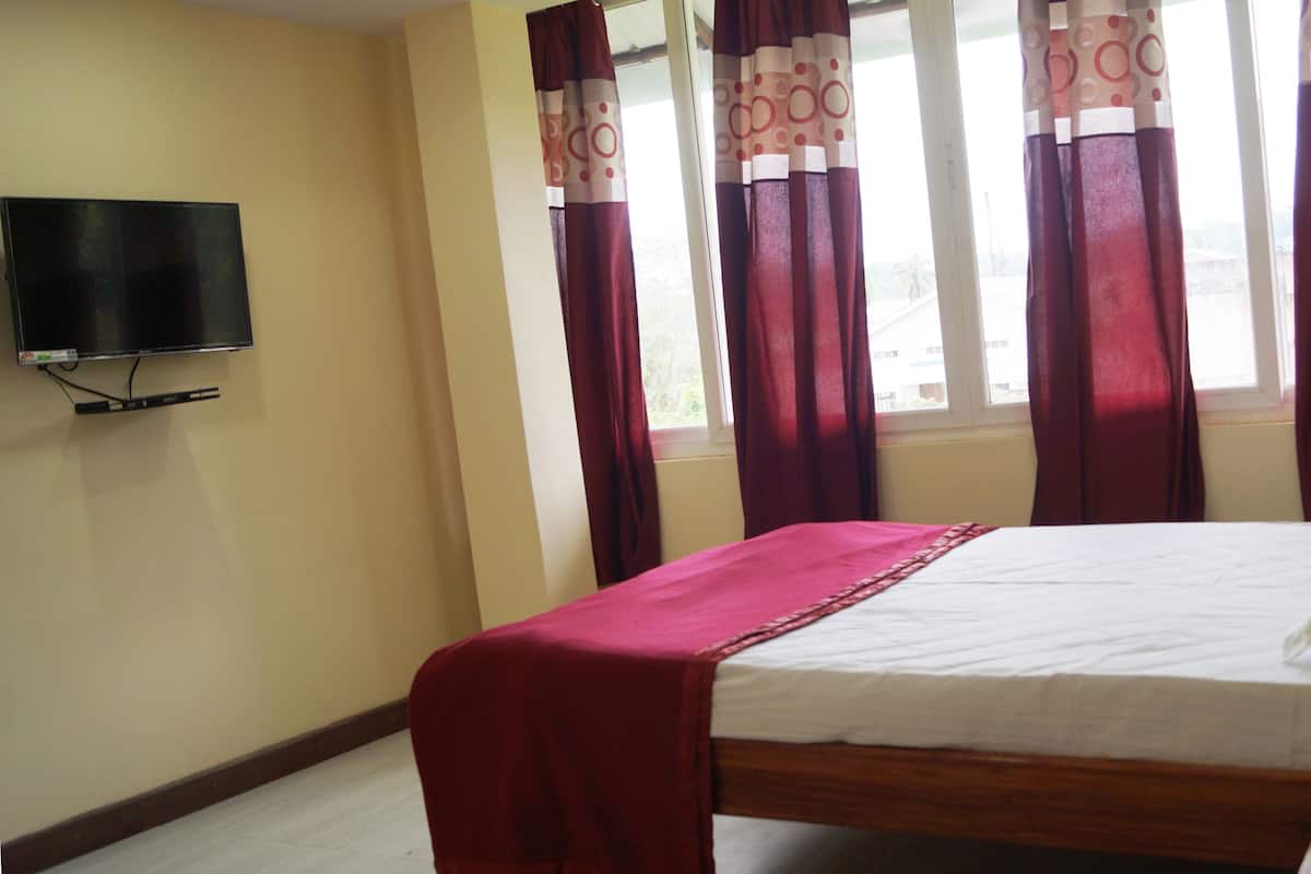 Quarto com cama, televisão na parede e janela com cortinas.