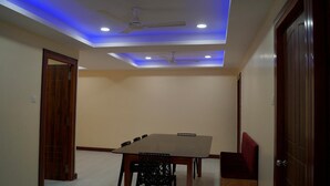A room with a dining table, chairs, a ceiling fan, recessed lighting, and a wooden door. - Sunnyvale Andaman (Port Blair)