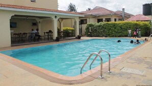 A swimming pool with a covered area and lounge chairs, surrounded by buildings and a hedge. - Bondo Pride Hotel (Bondo)