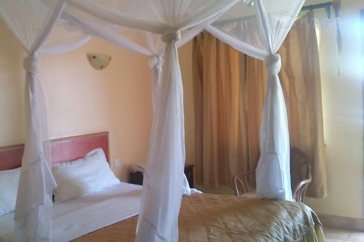 Una cama con dosel, una mesita de noche y una silla en una habitación con paredes color beige y cortinas.