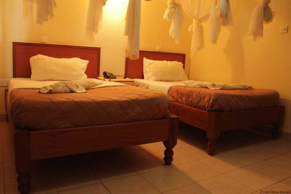 Habitación de hotel con dos camas, cabecera de madera, mesita de noche con lámpara y teléfono.