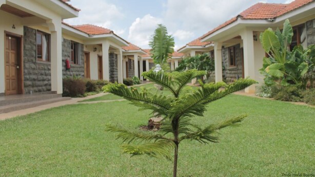 A row of two-story buildings with a consistent architectural style, featuring stone and stucco exteriors, and a central lawn with a small tree. - Bondo Pride Hotel (Bondo)