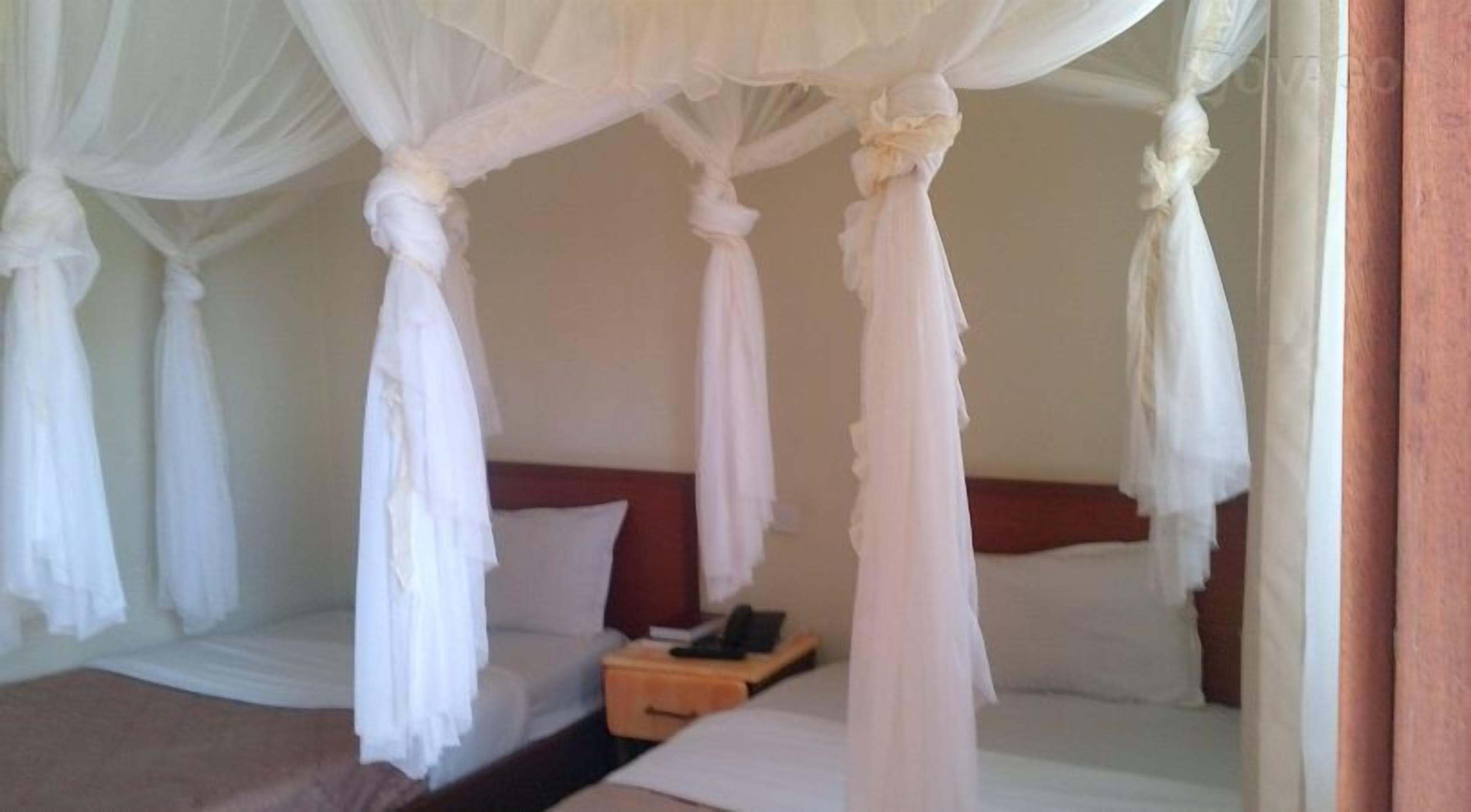 A bedroom with a canopy bed, a bedside table with a phone, and a red pillow.