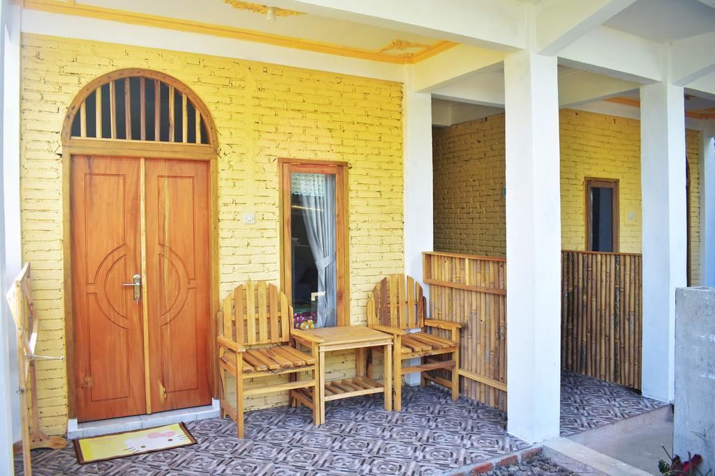 Una habitación con una puerta de madera, dos sillas de madera, una mesita y una ventana con cortina.