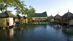 A traditional building with a green roof, surrounded by a water body and palm trees. - Cahaya Tetebatu Inn (Pringgasela)