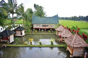 Una estructura tradicional con techo de paja y una plataforma central elevada, rodeada de agua y abundante vegetación.