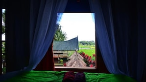 A bed with green bedding and a view of a thatched-roof structure through sheer curtains. - Cahaya Tetebatu Inn (Pringgasela)
