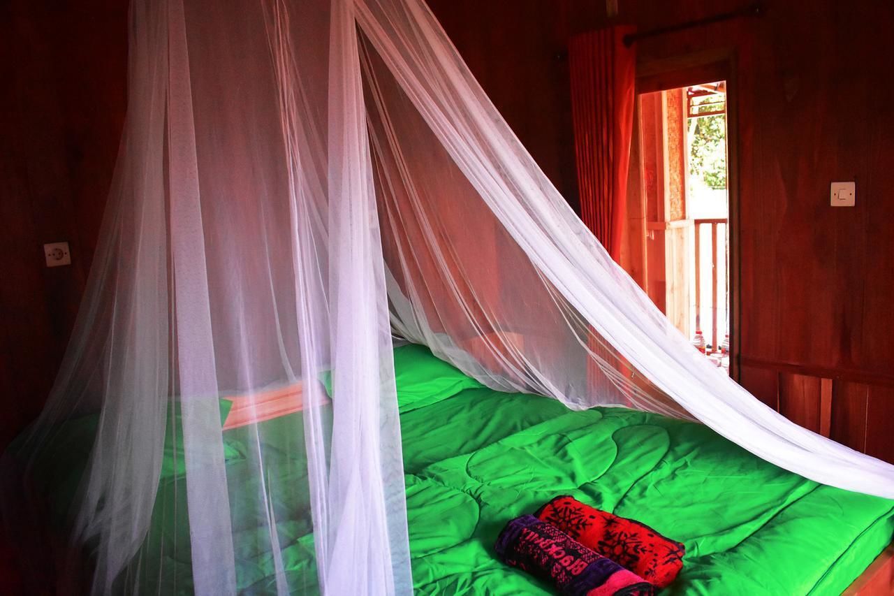 Una stanza con un letto coperto da un baldacchino bianco, una coperta verde e una porta rossa.