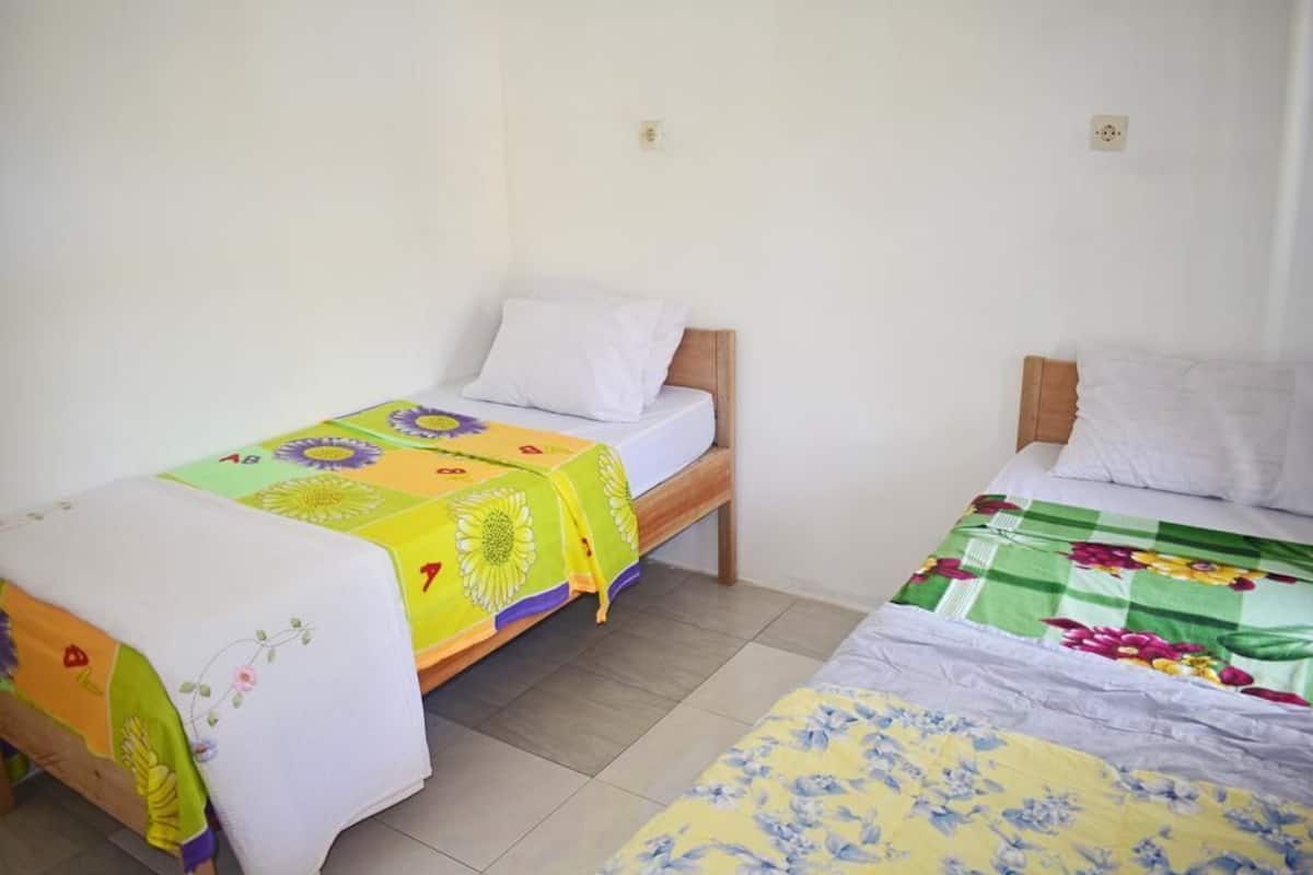Ein Zimmer mit zwei Einzelbetten, jeweils mit unterschiedlicher floraler Bettdecke, weißen Kissen und hölzernen Kopfteilen.