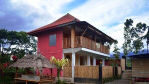 A two-story building with a red exterior, a balcony, and a thatched-roof structure nearby. - Cahaya Tetebatu Inn (Pringgasela)