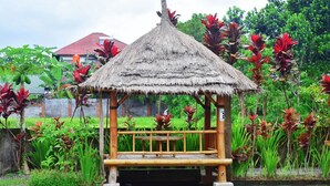 A thatched-roof gazebo with a bench, surrounded by lush greenery and red flowers. - Cahaya Tetebatu Inn (Pringgasela)