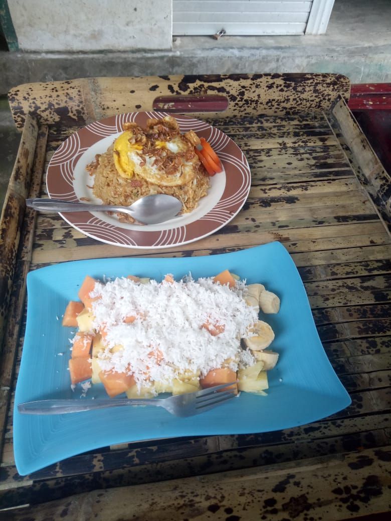 Una mesa de madera rústica con dos platos de comida, uno con un huevo frito y verduras, y otro con frutas y coco.