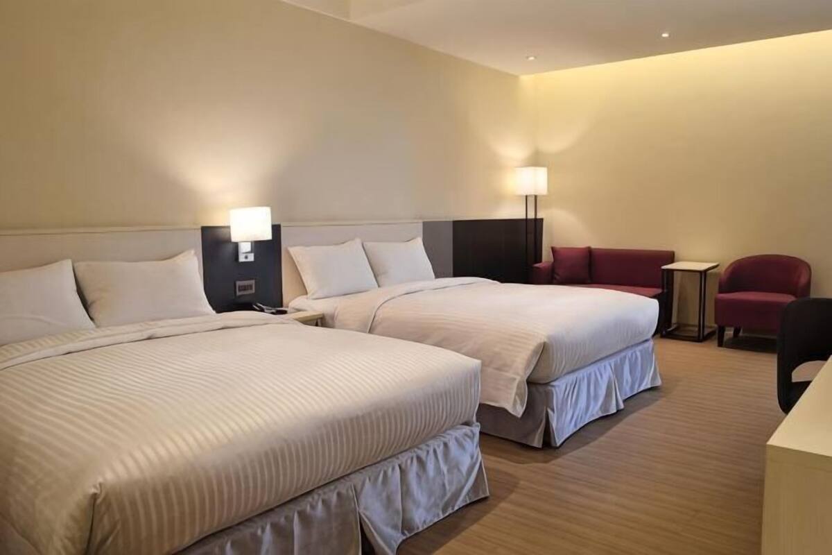 Ein Hotelzimmer mit zwei Betten, einem Schreibtisch, einem Stuhl und einer Lampe.