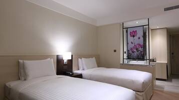 A hotel room with two beds, a nightstand, a lamp, a mirror with a floral design, and a bathroom with a sink and mirror.