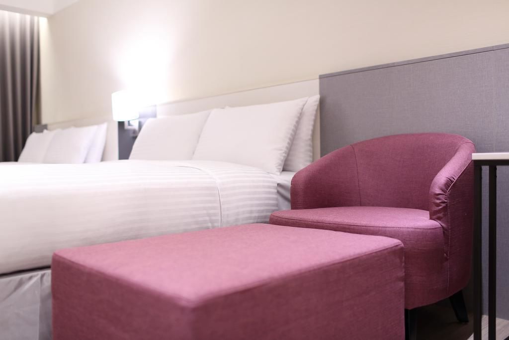 A hotel room with a bed, a pink armchair, and a small table.