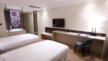 Une chambre d’hôtel avec deux lits, un bureau, une chaise, une télévision et une grande fenêtre ornée d’un tableau représentant des motifs floraux.