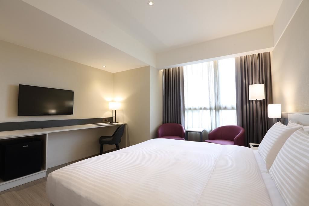 A hotel room with a large bed, a desk with a chair, a television, and two lamps.