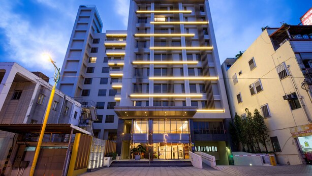 Un hotel moderno con una entrada destacada, varios pisos y señalización iluminada.