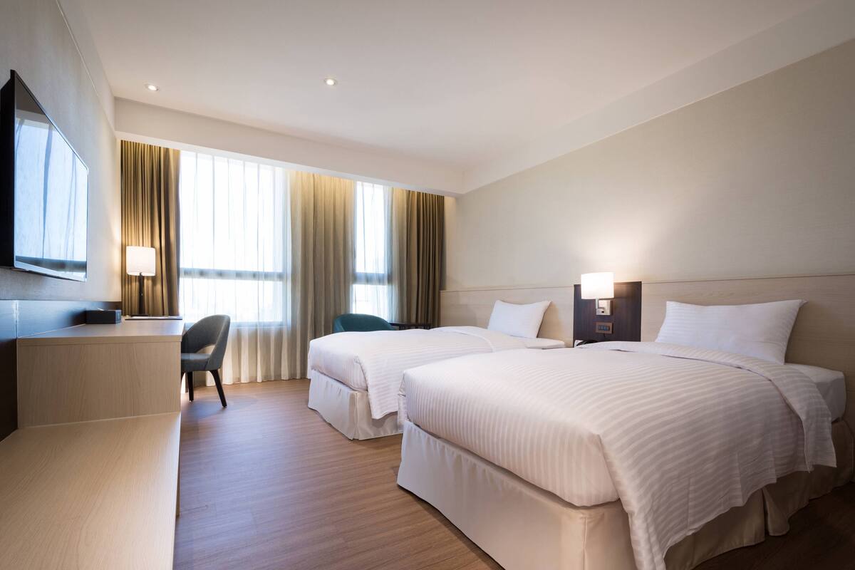 Ein Hotelzimmer mit zwei Betten, einem Schreibtisch, einem Stuhl und einem Fernseher.