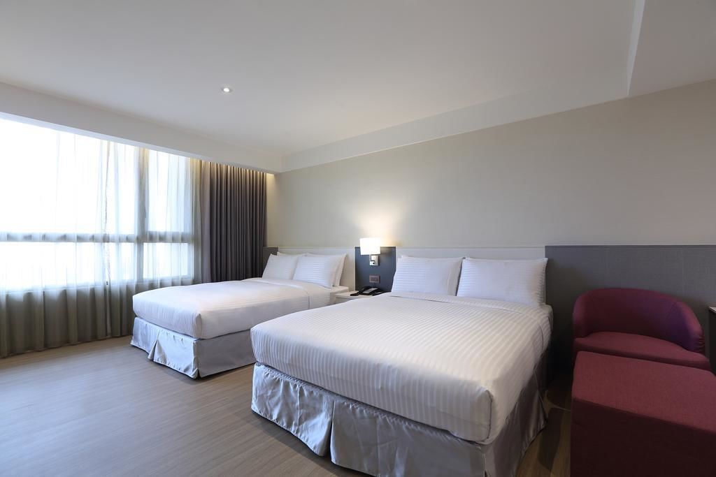 Une chambre d’hôtel avec deux lits, un bureau, une chaise et une grande fenêtre avec des rideaux.