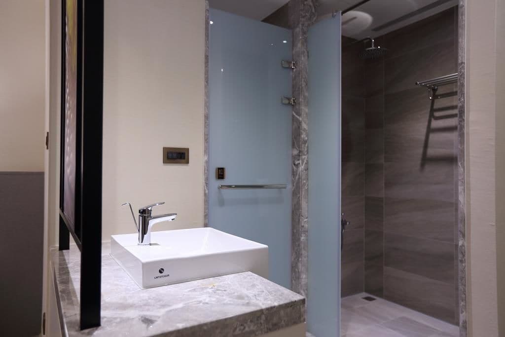 Une salle de bain moderne avec un lavabo blanc, une douche en verre et des comptoirs en marbre.