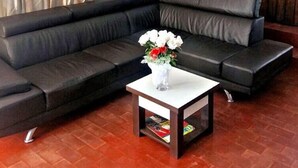 A modern living room with a black leather sofa, a white coffee table with a vase of flowers, and a fire extinguisher on the wall. - Hotel Bilene (Praia do Bilene)