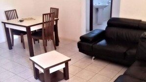 A living room with a black leather sofa, a dining table with four chairs, and a small white table. - Hotel Bilene (Praia do Bilene)