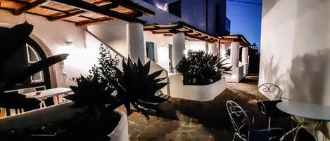Un patio con pérgola, plantas en macetas y mobiliario de exterior.