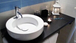 Uma pia branca com uma torneira moderna em uma bancada preta em um banheiro.