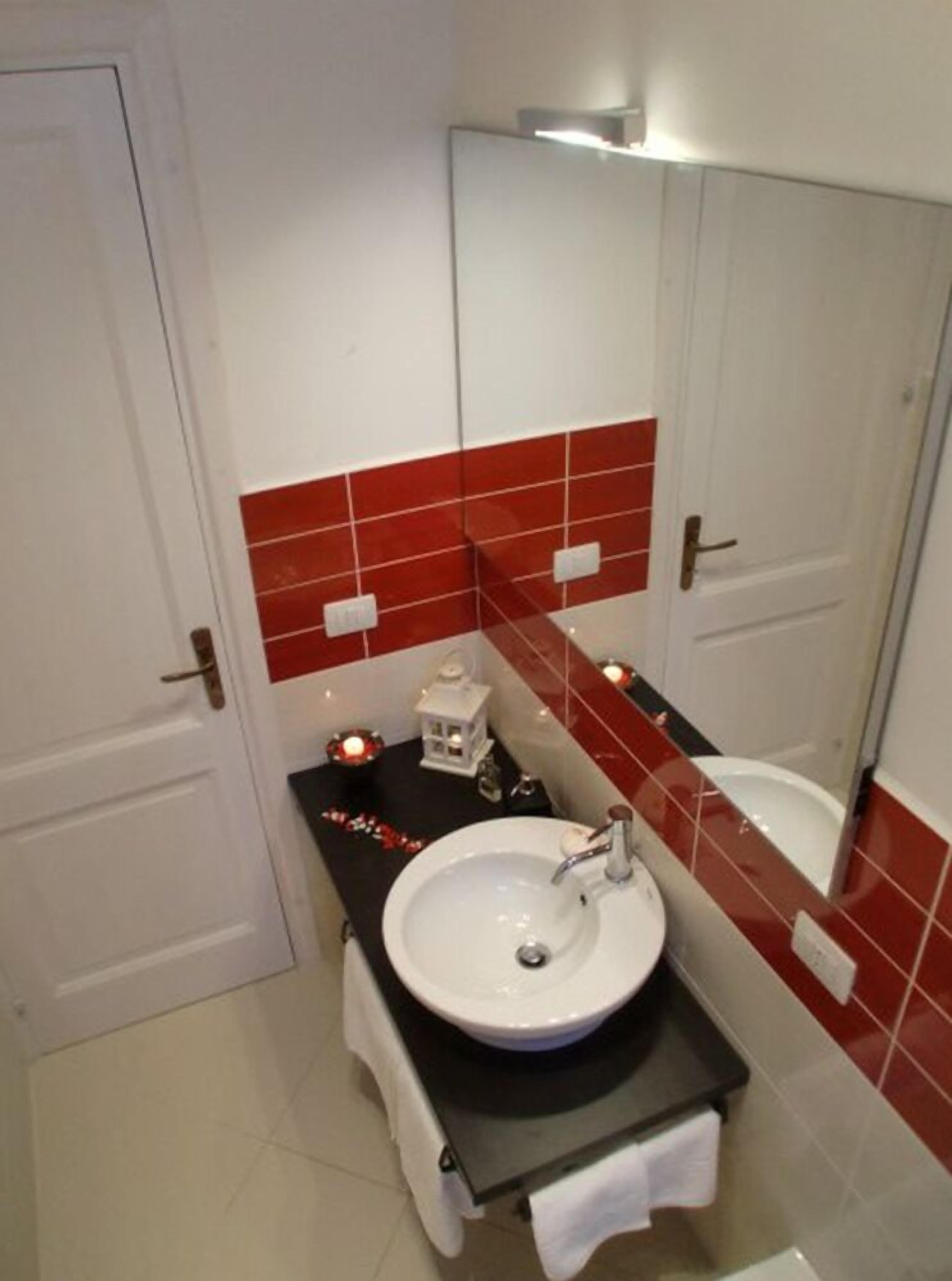 A bathroom with a white sink, red-tiled walls, a mirror, and a small decorative lantern.
