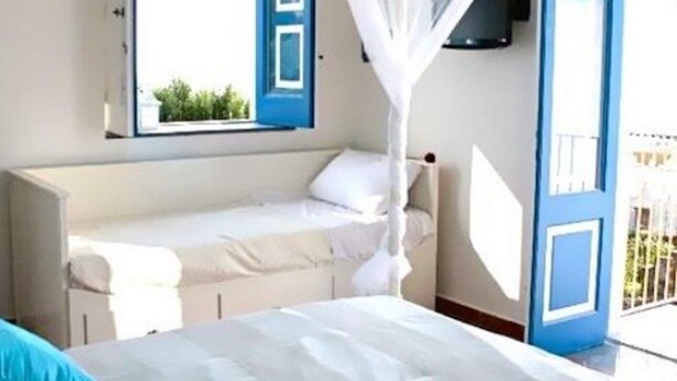Quarto com cama, janela com persianas azuis e porta para varanda.