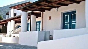 Um edifício moderno com fachada branca, portas azuis e uma área externa coberta com piso de pedra.