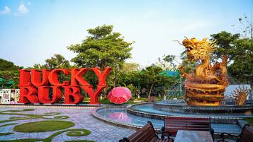 A park with a large 'Lucky Ruby' sign, a golden dragon fountain, and a patterned tiled area with benches.