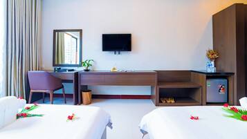 A hotel room with a desk, chair, two beds, a TV, a small fridge, and a window with curtains.