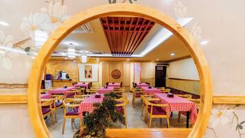 Restaurante com mesas redondas cobertas por toalhas xadrez vermelhas e brancas, cadeiras de madeira e um elemento decorativo central.