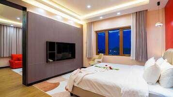 A modern hotel room with a large bed, a flat-screen TV mounted on the wall, a window with curtains, and a red sofa in the corner.
