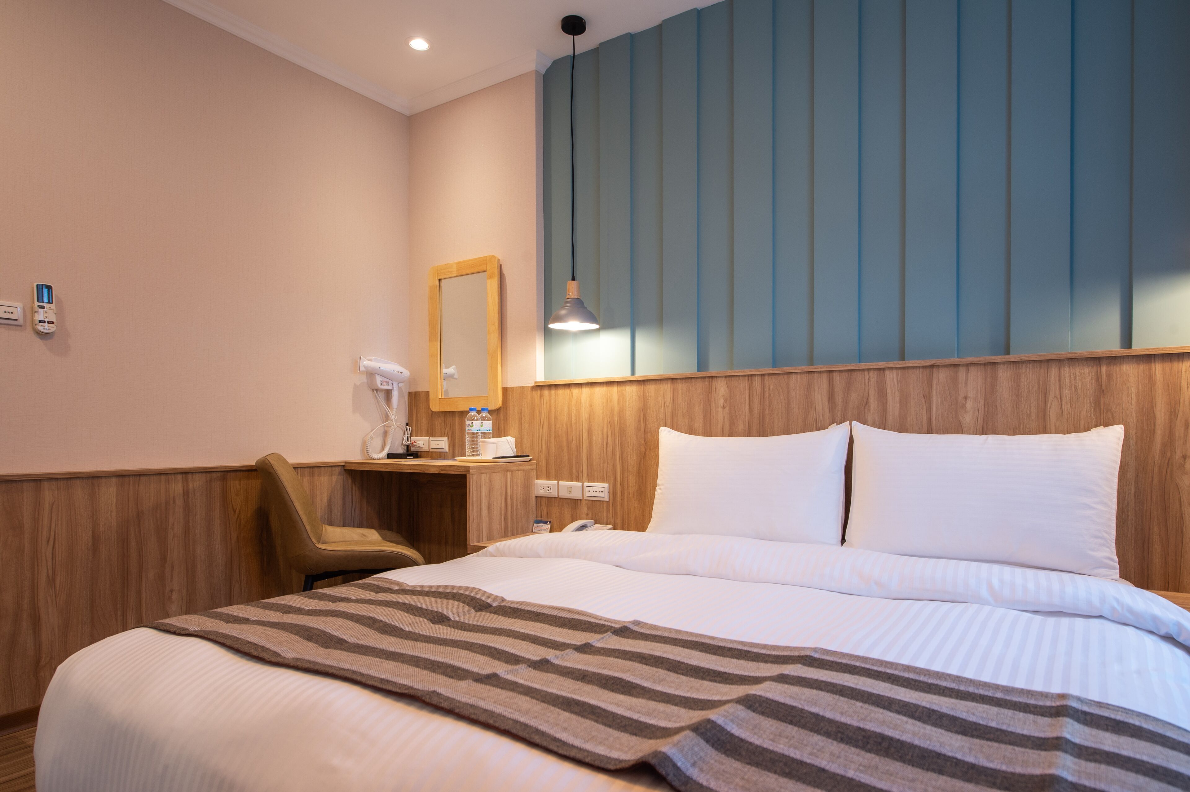 Hotelkamer met een groot bed, een houten hoofdbord, nachtkastje met een lamp, een stoel en een spiegel.