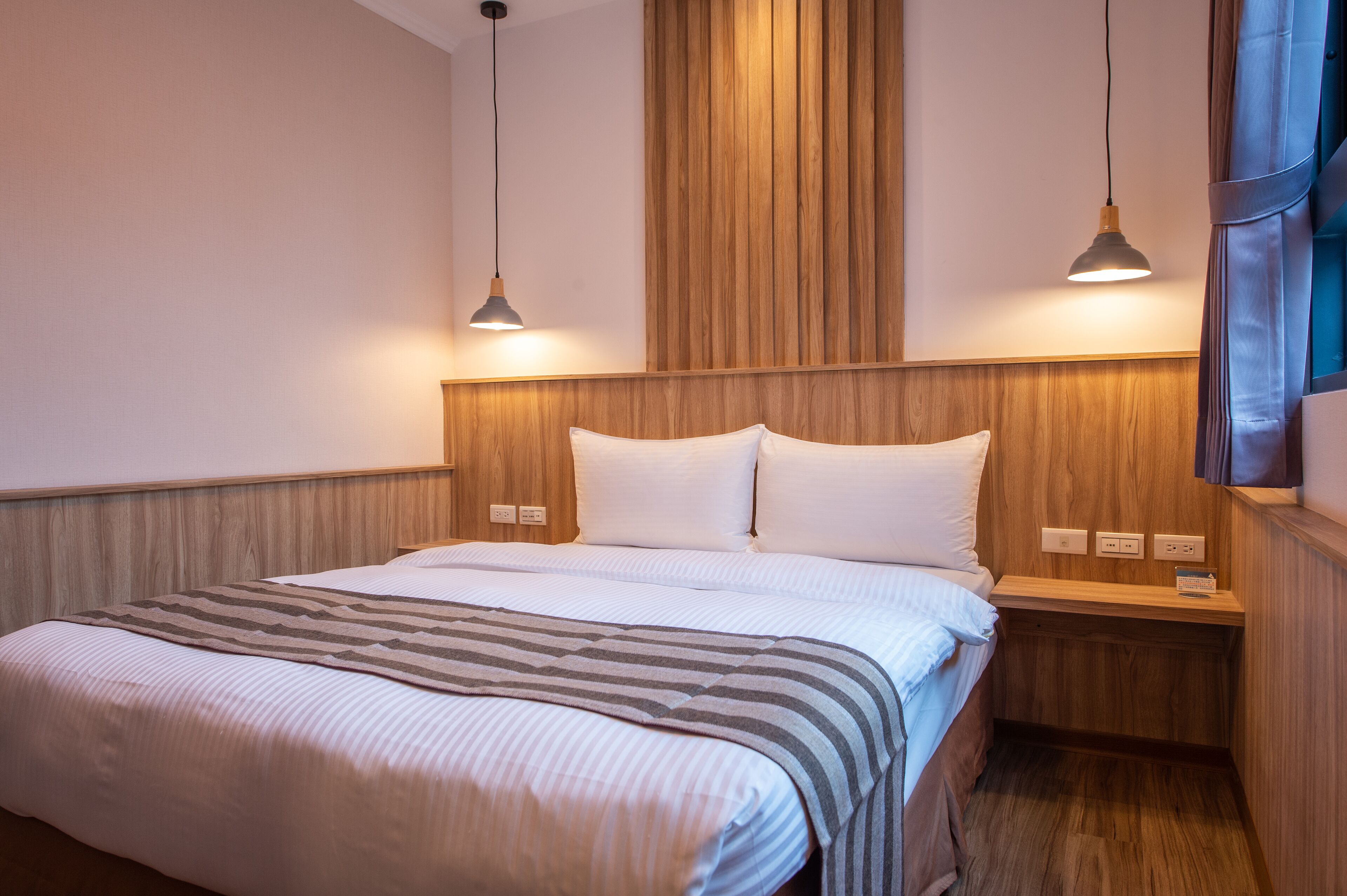 A neatly made bed with a striped blanket, wooden headboard, and bedside tables with lamps.
