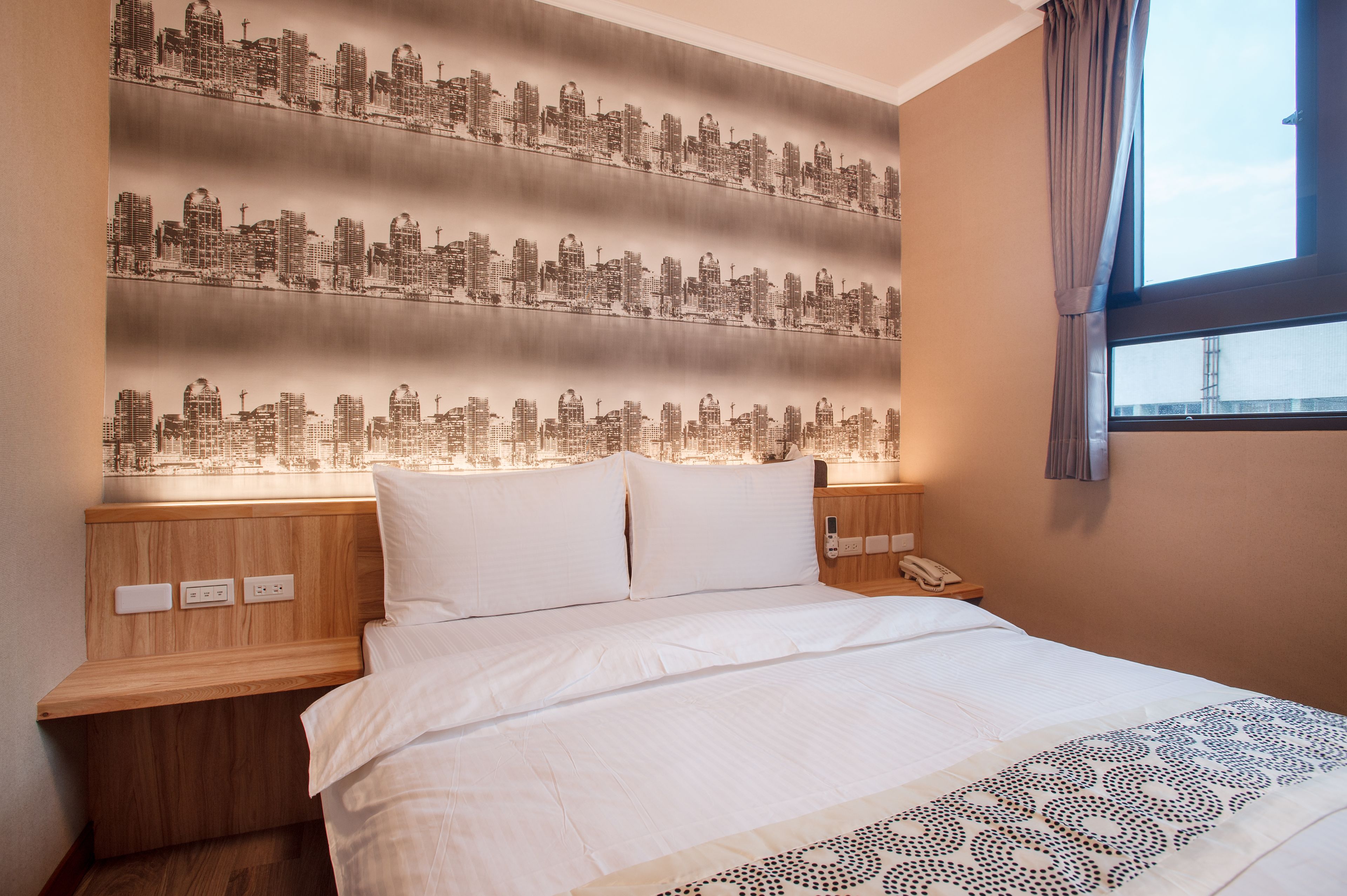 Ein Hotelzimmer mit einem großen Bett, Stadtkulissen-Tapete, einem Holz-Kopfteil, Nachttischen und einem Fenster mit Vorhängen.