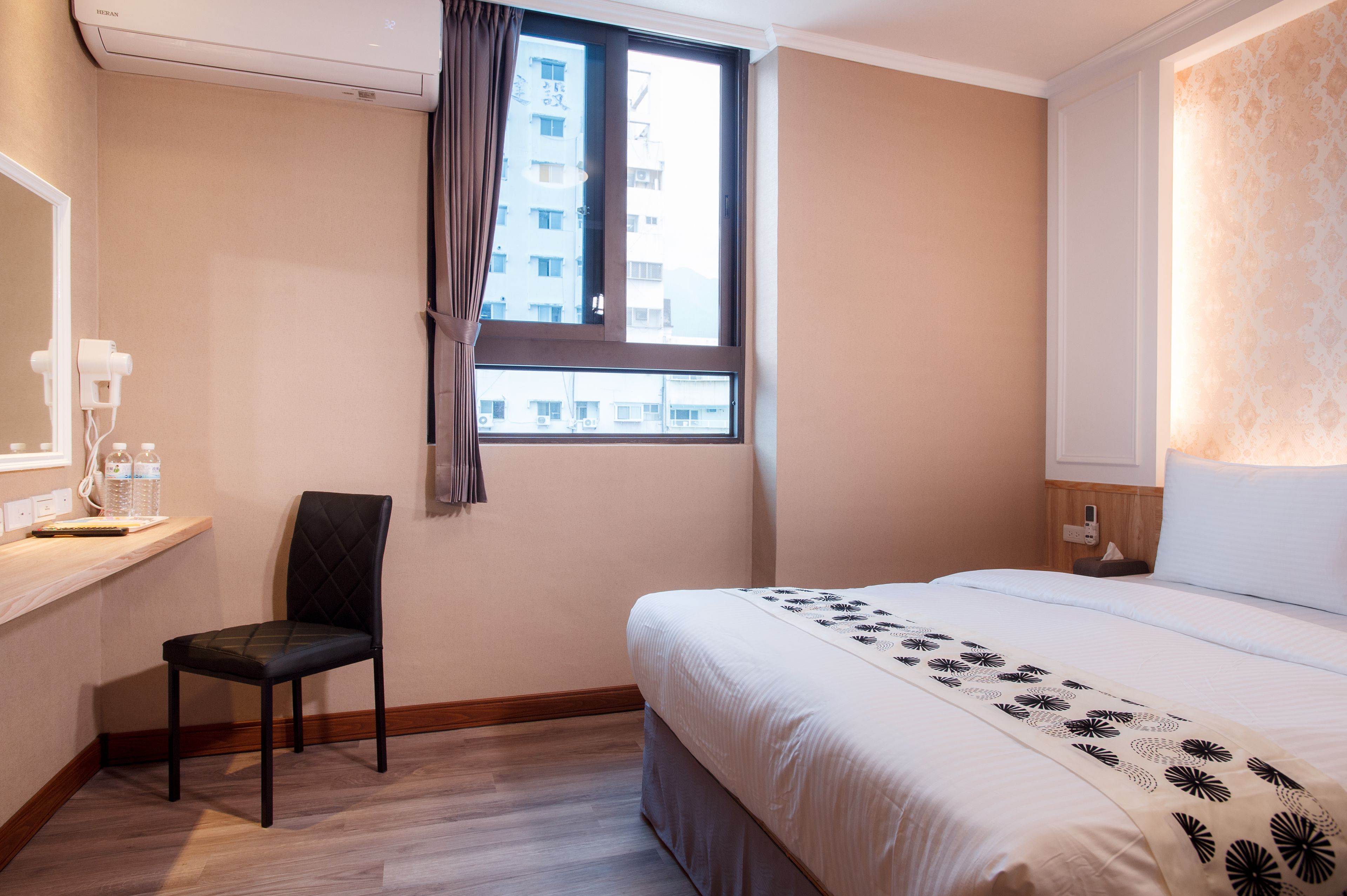 Una camera d'albergo con un letto, una sedia, una scrivania con uno specchio e una finestra vista edifici.