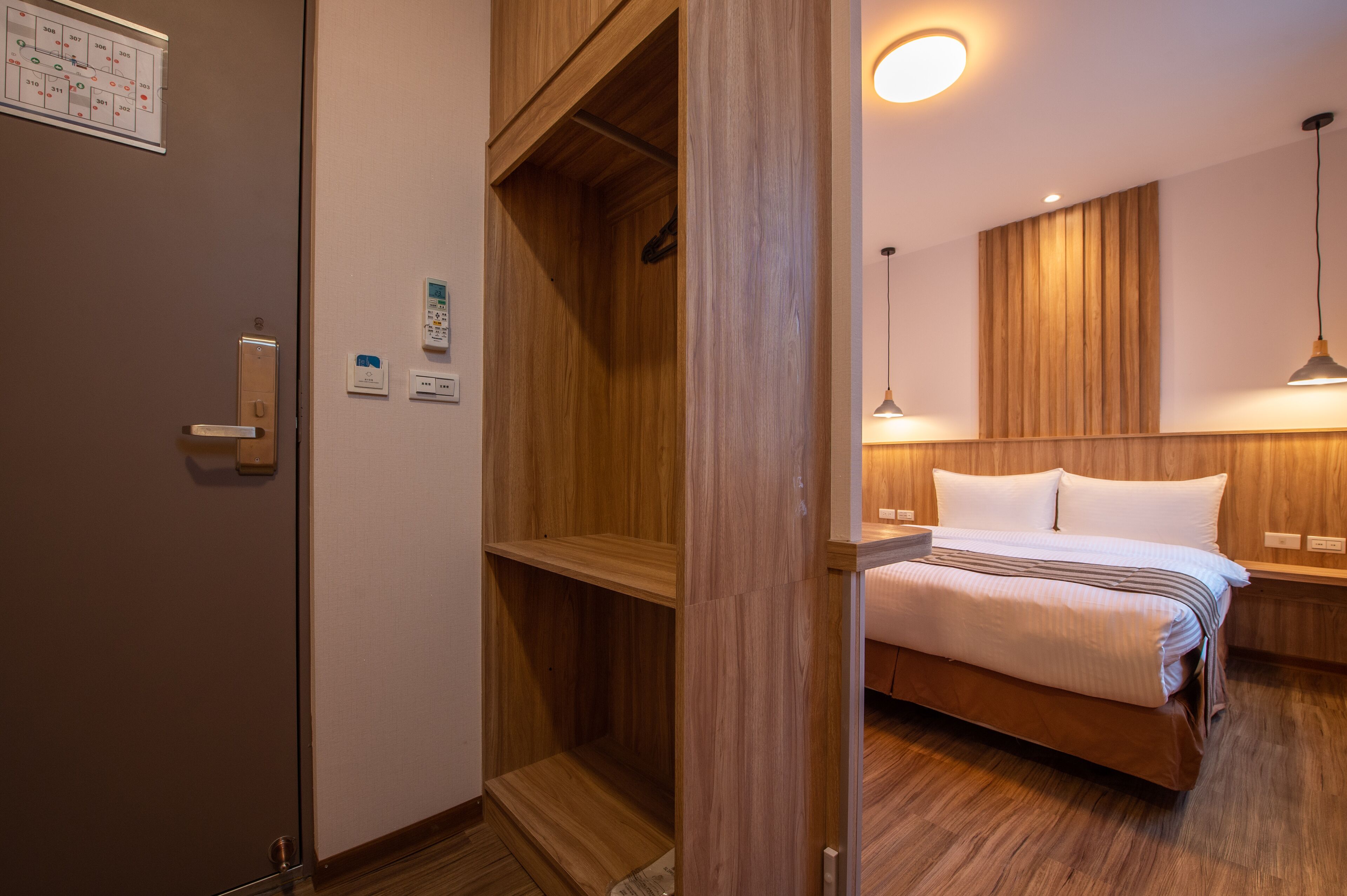 A hotel room with a wooden wardrobe, a bed with white bedding, and a pendant light.